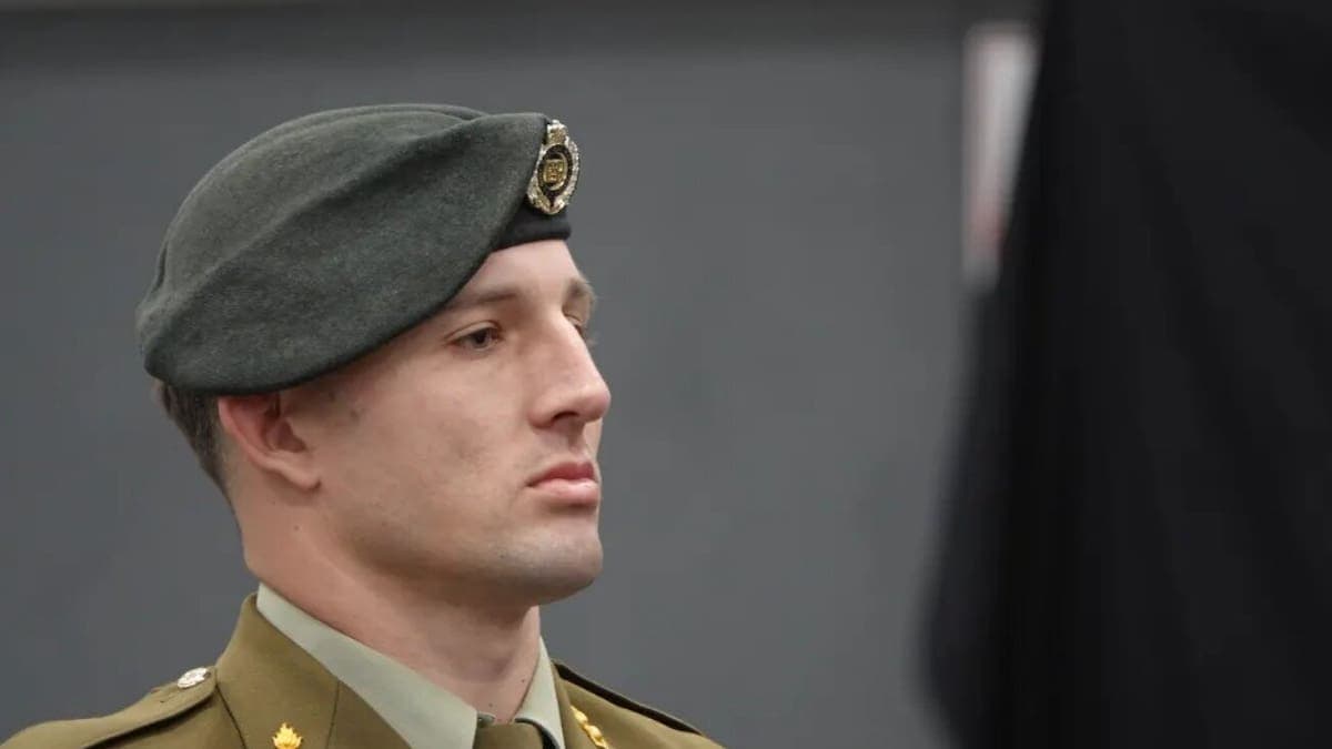 Uniformed New Zealand soldier standing outside Waiouru Military Camp with a backdrop of training facilities
